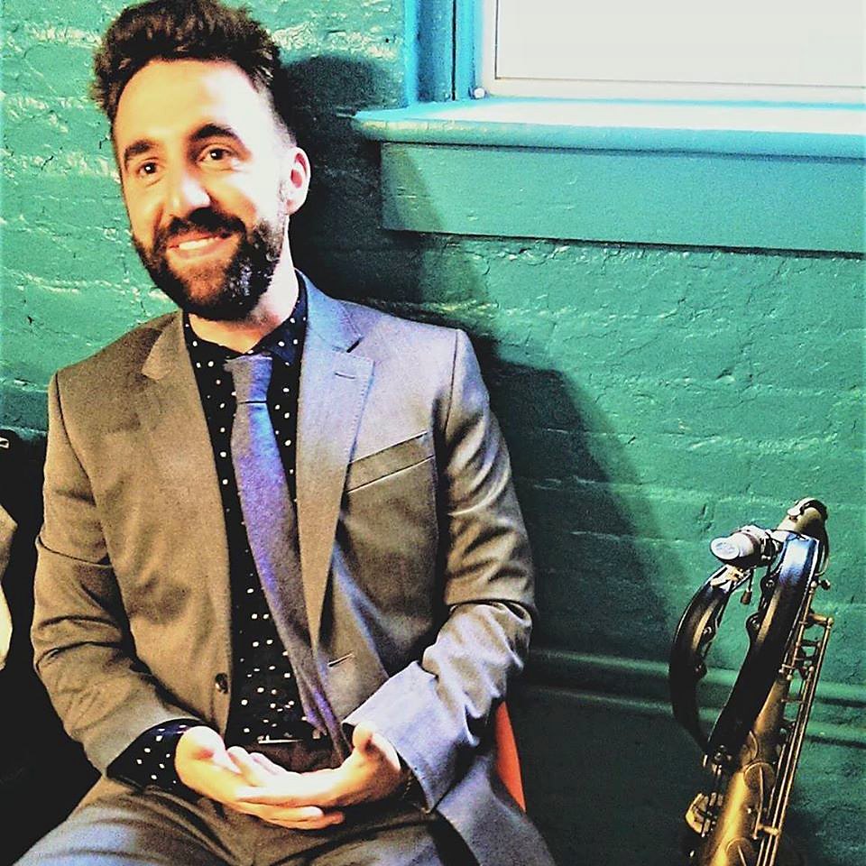 Jeff Fennell seated beside his tenor saxophone, smiling