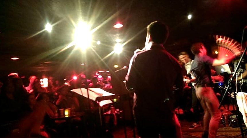 A packed club in Boston, MA, seen from the stage under bright lights